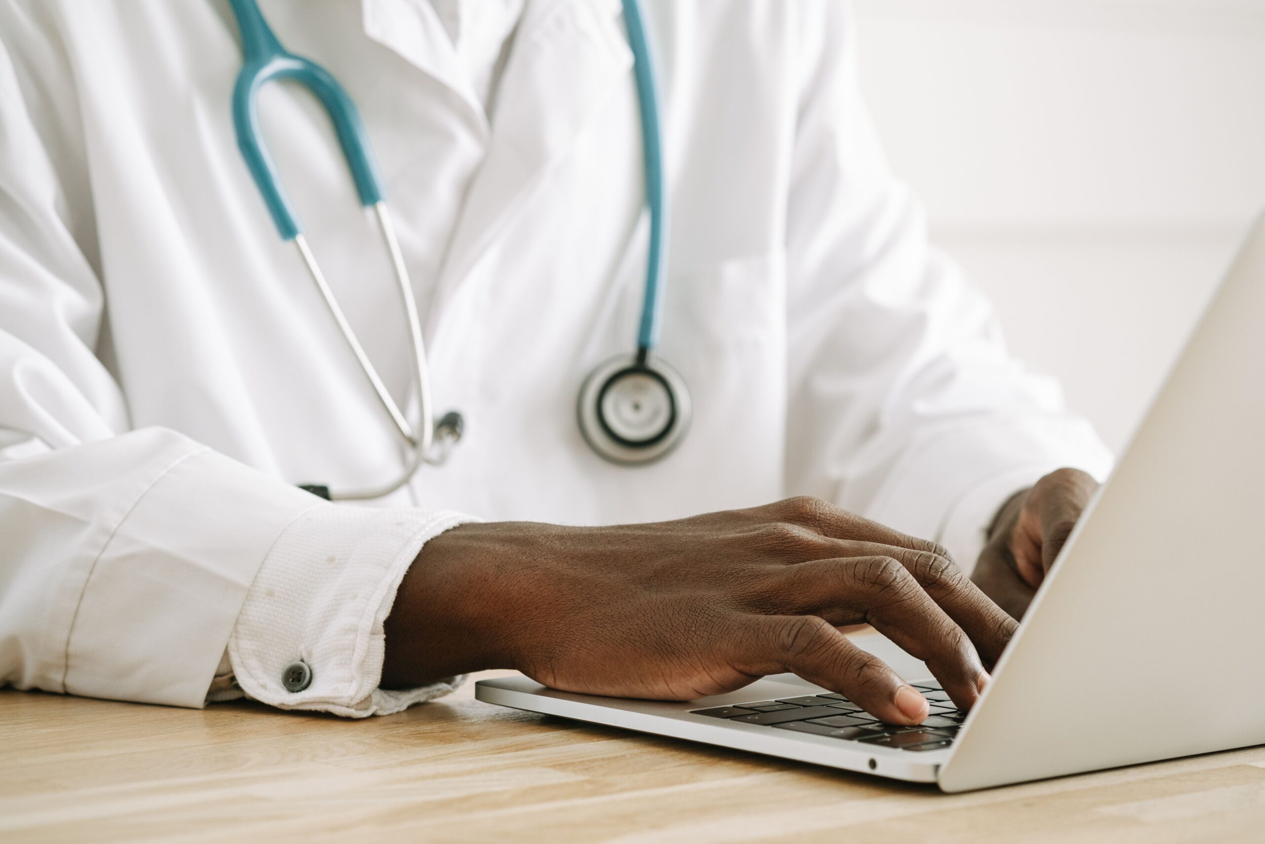 Doctor typing consultation notes on a laptop, a task an AI medical scribe can help draft